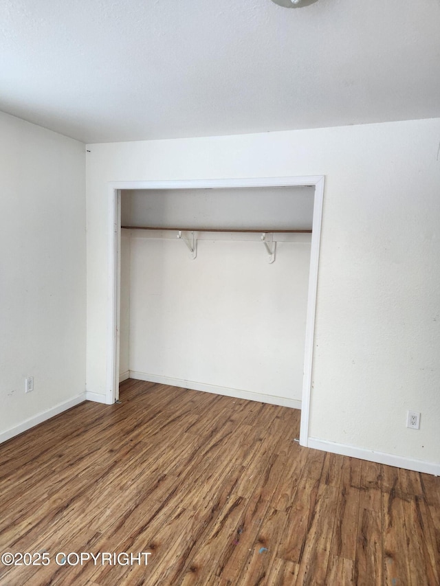 unfurnished bedroom featuring a closet, baseboards, and wood finished floors