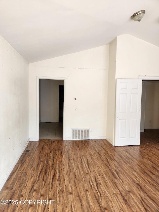 unfurnished room with baseboards, visible vents, vaulted ceiling, and wood finished floors