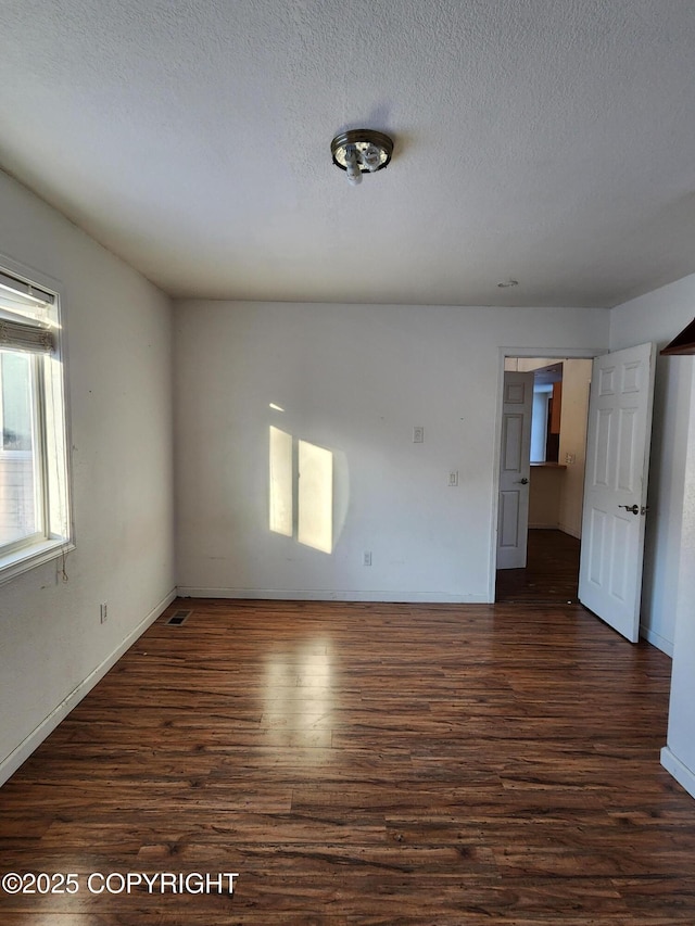 unfurnished room with baseboards, a textured ceiling, visible vents, and dark wood-type flooring