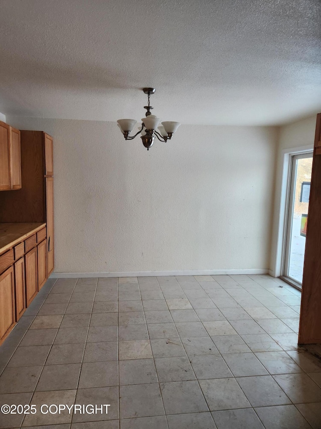 unfurnished dining area with baseboards, a chandelier, a textured ceiling, and a textured wall