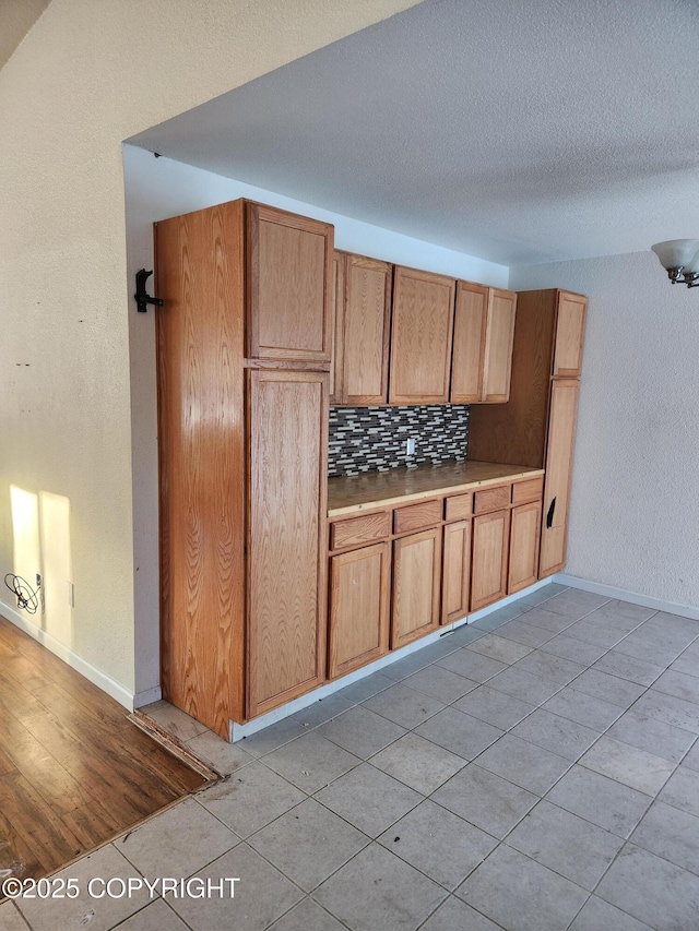 kitchen with baseboards, decorative backsplash, a textured ceiling, and light countertops