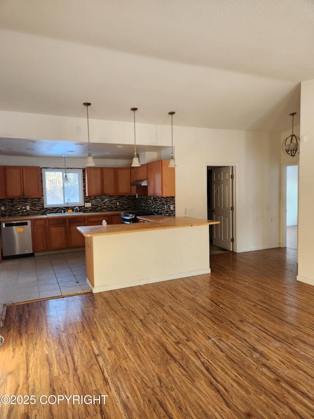 kitchen featuring brown cabinetry, wood finished floors, decorative light fixtures, stainless steel appliances, and backsplash