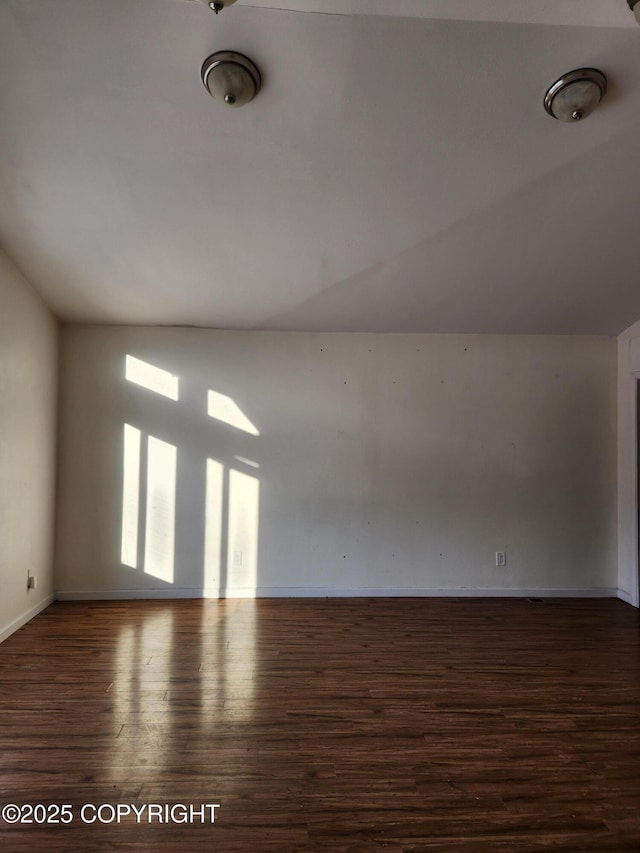 empty room featuring lofted ceiling, wood finished floors, and baseboards