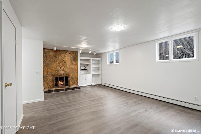 521 N St, Anchorage, AK 99501 - unfurnished living room with rail lighting, baseboard heating, baseboards, a stone fireplace, and wood finished floors