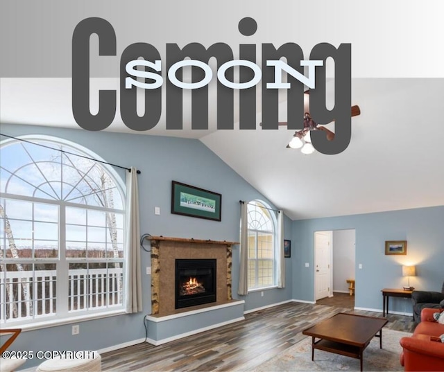 living room featuring a warm lit fireplace, vaulted ceiling, baseboards, and wood finished floors