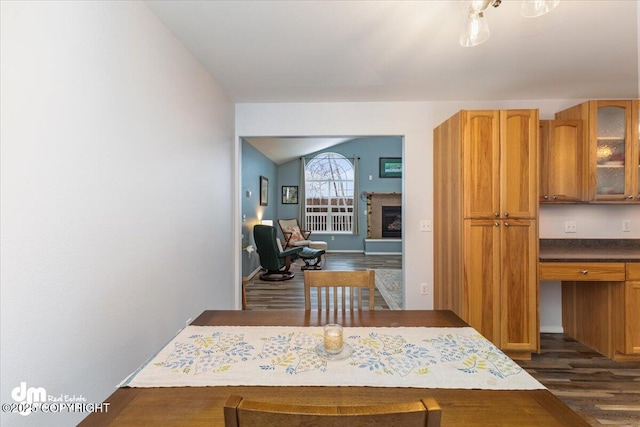 dining area featuring dark wood-type flooring, lofted ceiling, and a glass covered fireplace