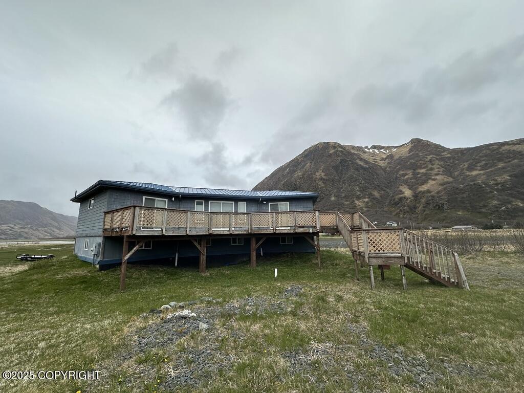 rear view of house with a deck with mountain view, metal roof, a yard, and stairway