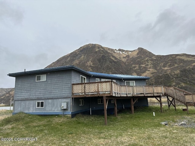 rear view of property featuring metal roof, a deck with mountain view, a lawn, and stairs