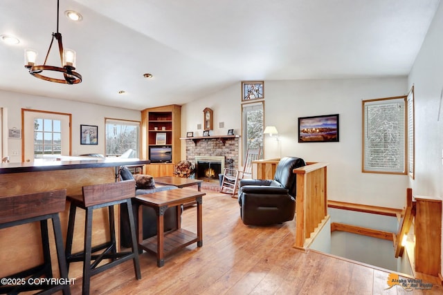 living area with light wood finished floors, an inviting chandelier, a brick fireplace, and lofted ceiling