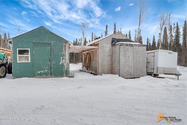 snow covered structure with a storage unit and an outbuilding