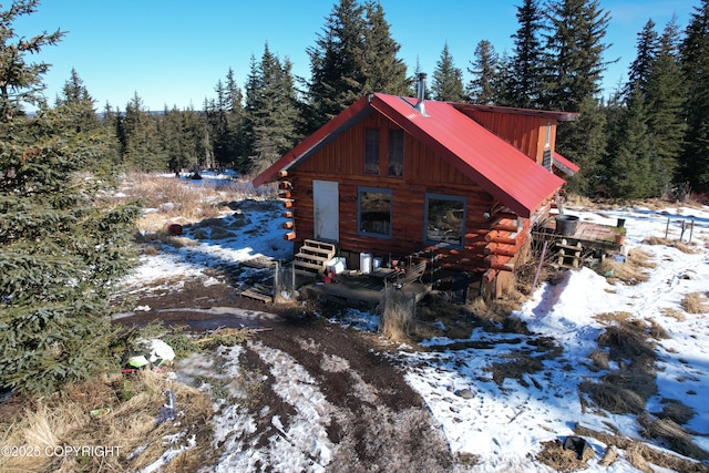 snow covered property featuring log siding, entry steps, metal roof, and a view of trees