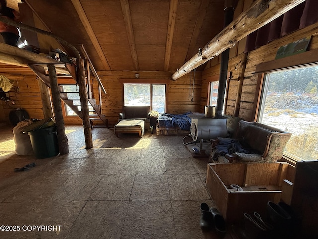 interior space featuring stairway, wooden walls, a wood stove, and vaulted ceiling