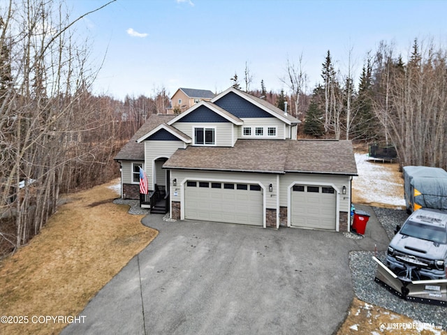 view of front of home with driveway, roof with shingles, a garage, stone siding, and a trampoline