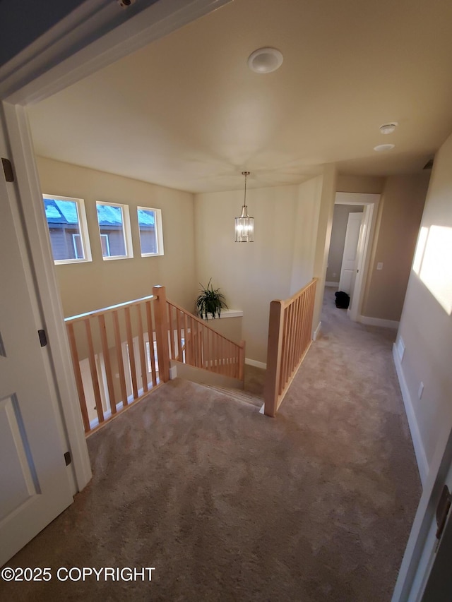 hallway featuring carpet, baseboards, an upstairs landing, and an inviting chandelier