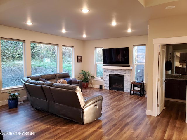 living room featuring recessed lighting, a stone fireplace, baseboards, and wood finished floors