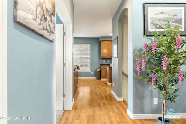 corridor with light wood finished floors, arched walkways, and baseboards