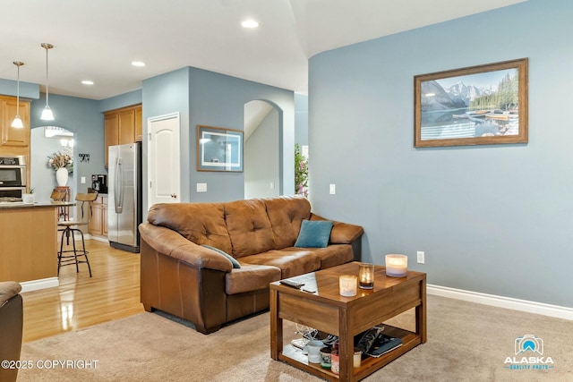 living area featuring light carpet, recessed lighting, arched walkways, light wood finished floors, and baseboards