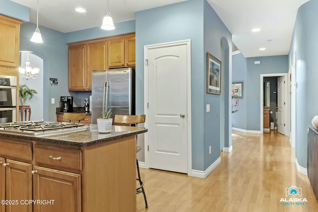 kitchen featuring light wood-type flooring, stainless steel appliances, arched walkways, dark stone counters, and baseboards