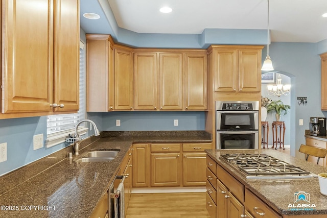 kitchen featuring a kitchen island, stainless steel appliances, hanging light fixtures, a sink, and light wood-type flooring