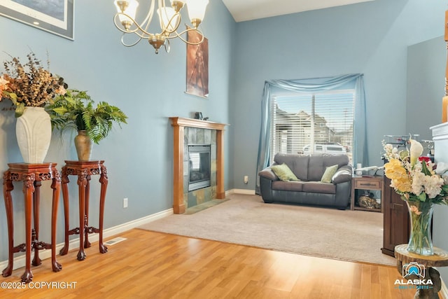 living area featuring a tiled fireplace, visible vents, a chandelier, and wood finished floors