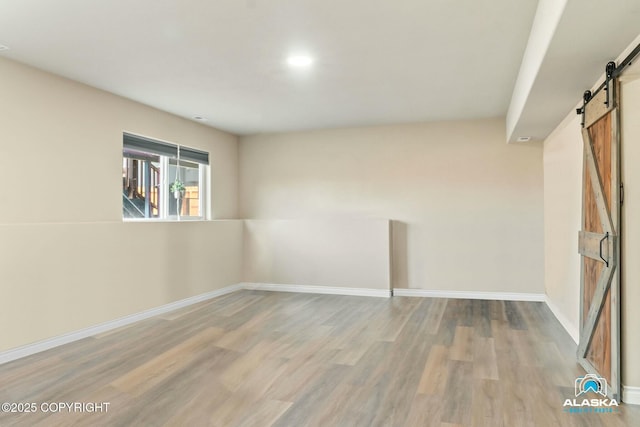 empty room featuring a barn door, wood finished floors, and baseboards