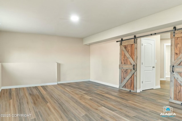 below grade area featuring a barn door, baseboards, and wood finished floors