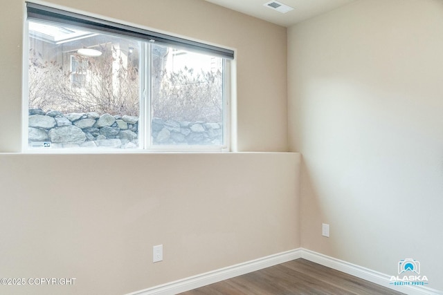 empty room featuring visible vents, dark wood-type flooring, and baseboards