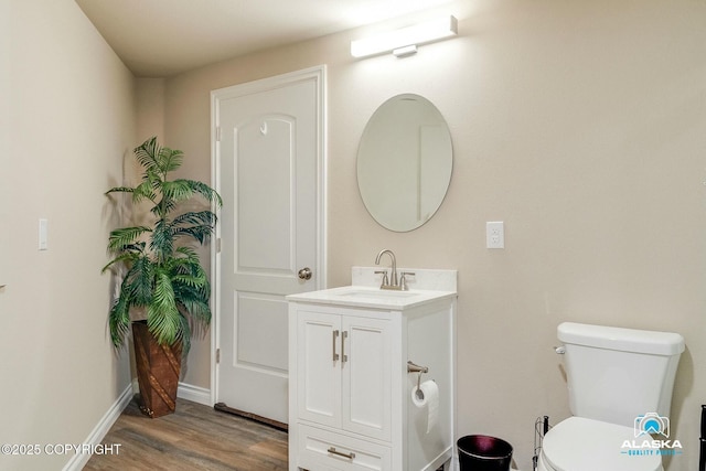 half bathroom featuring vanity, toilet, wood finished floors, and baseboards