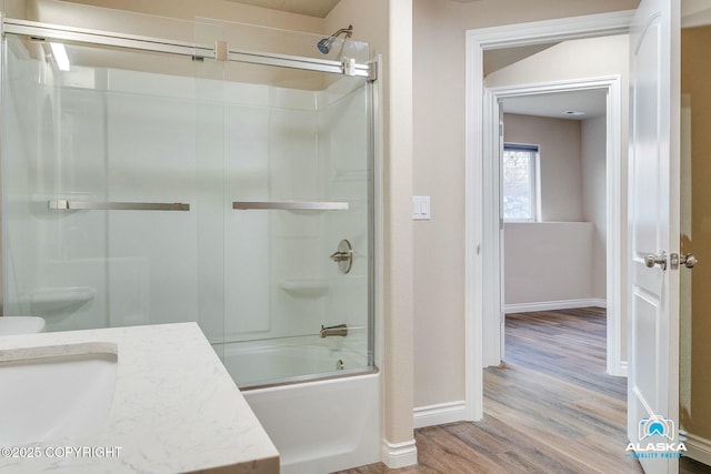 bathroom featuring combined bath / shower with glass door, baseboards, wood finished floors, and vanity