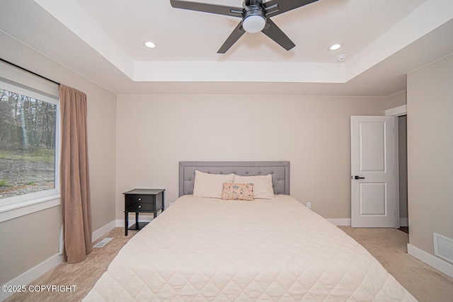 bedroom with a tray ceiling, light colored carpet, visible vents, and baseboards