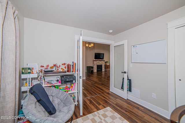 interior space featuring a stone fireplace, a notable chandelier, wood finished floors, visible vents, and baseboards