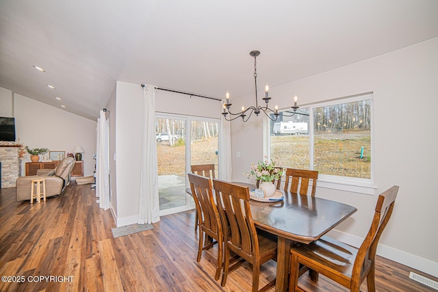 dining space featuring visible vents, vaulted ceiling, a stone fireplace, and wood finished floors