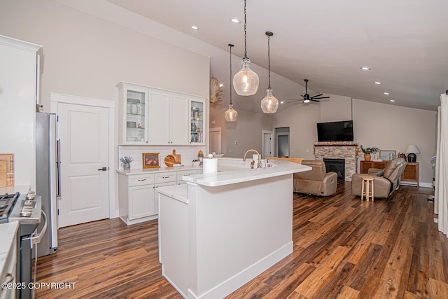 kitchen with white cabinets, dark wood-style floors, hanging light fixtures, stainless steel appliances, and a stone fireplace