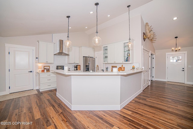 kitchen with dark wood-style floors, high end fridge, light countertops, glass insert cabinets, and wall chimney range hood