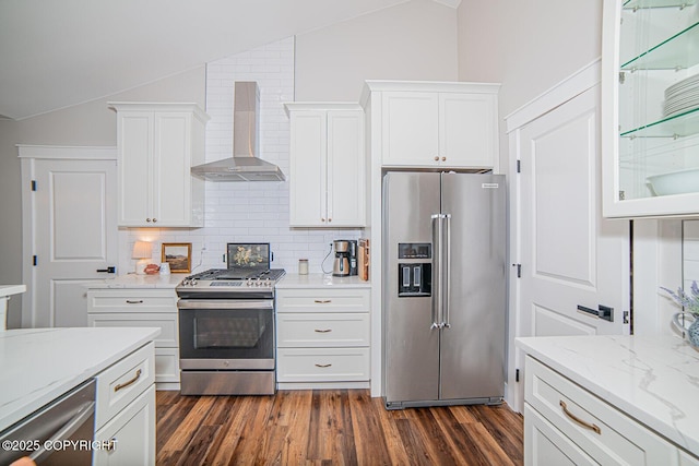 kitchen with lofted ceiling, stainless steel appliances, wall chimney range hood, and white cabinetry