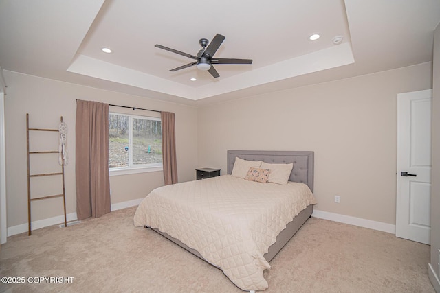 bedroom featuring light carpet, a tray ceiling, and baseboards