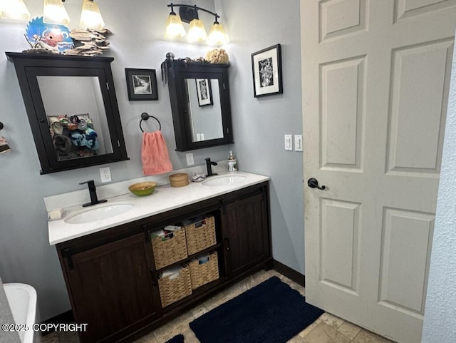 bathroom with double vanity, stone finish floor, a sink, and baseboards