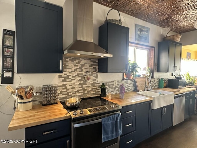 kitchen with an ornate ceiling, wall chimney exhaust hood, appliances with stainless steel finishes, and wooden counters