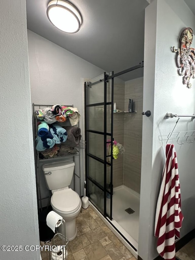 bathroom featuring stone finish floor, a textured wall, a stall shower, and toilet