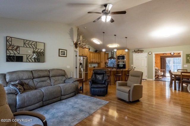 living room featuring light wood-type flooring, a ceiling fan, and vaulted ceiling