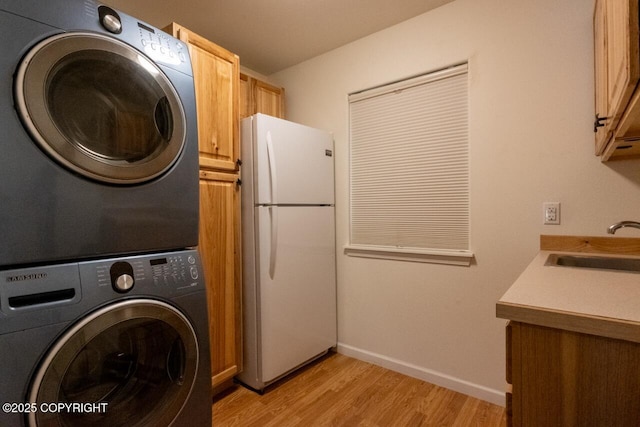 laundry area featuring a sink, stacked washing maching and dryer, cabinet space, light wood-style floors, and baseboards