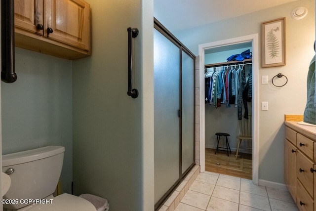 bathroom with a walk in closet, toilet, a stall shower, tile patterned floors, and vanity