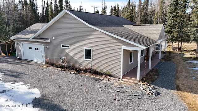 view of side of home with gravel driveway, an attached garage, and a shingled roof