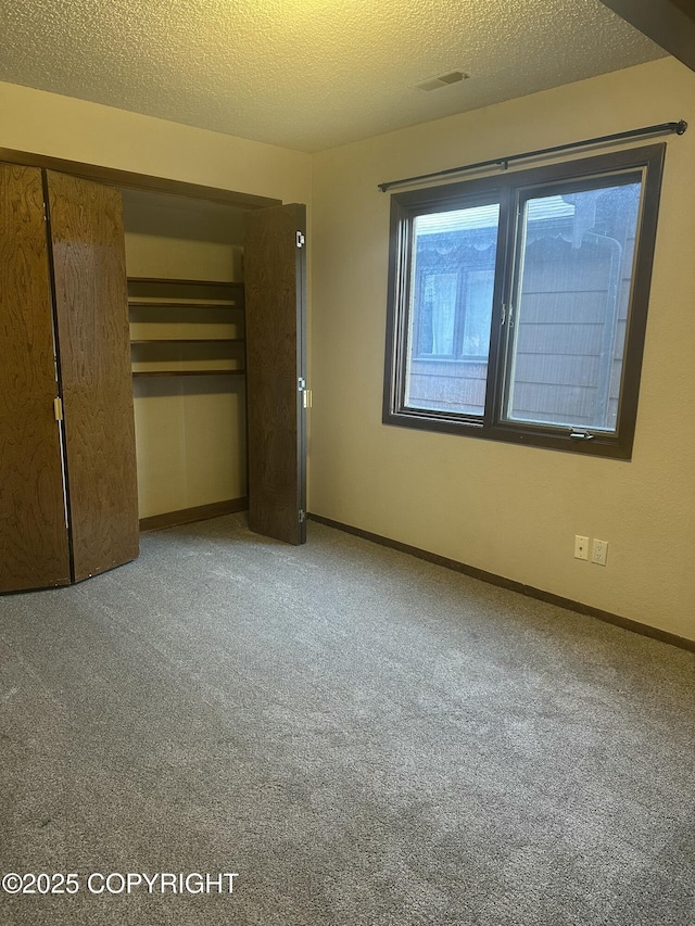 unfurnished bedroom featuring baseboards, visible vents, a textured ceiling, carpet flooring, and a closet