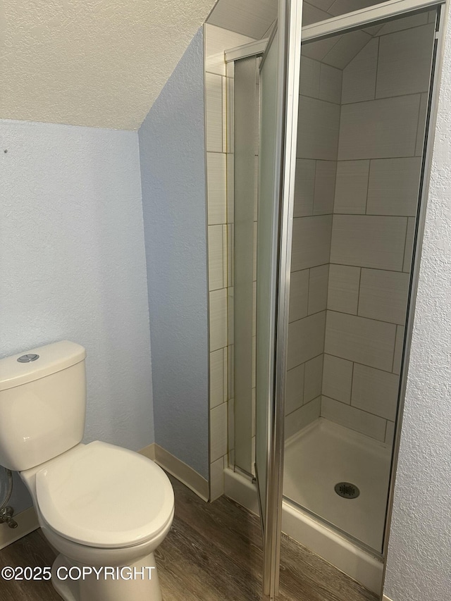 full bath with a stall shower, a textured wall, toilet, and wood finished floors