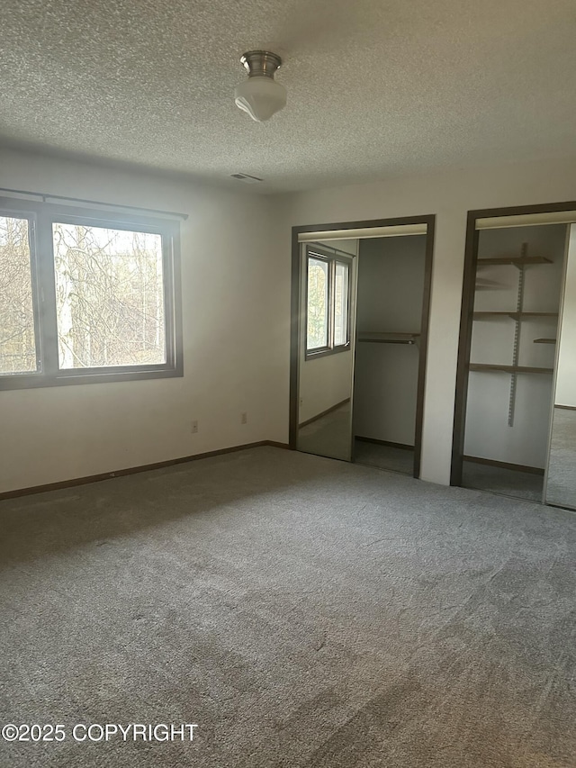 unfurnished bedroom with a textured ceiling, visible vents, baseboards, multiple closets, and carpet