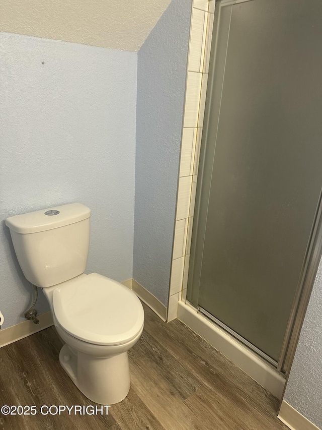 bathroom with a textured wall, toilet, wood finished floors, baseboards, and a stall shower