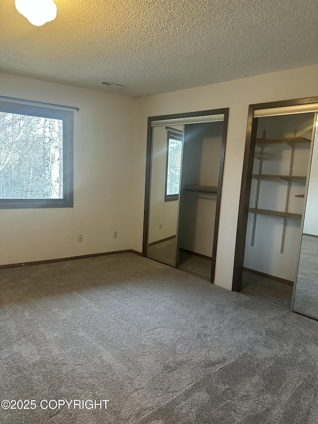 unfurnished bedroom featuring multiple closets, carpet flooring, visible vents, and a textured ceiling