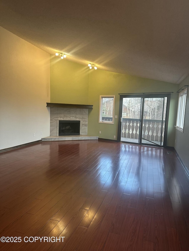 unfurnished living room featuring lofted ceiling, dark wood-type flooring, a tile fireplace, and baseboards