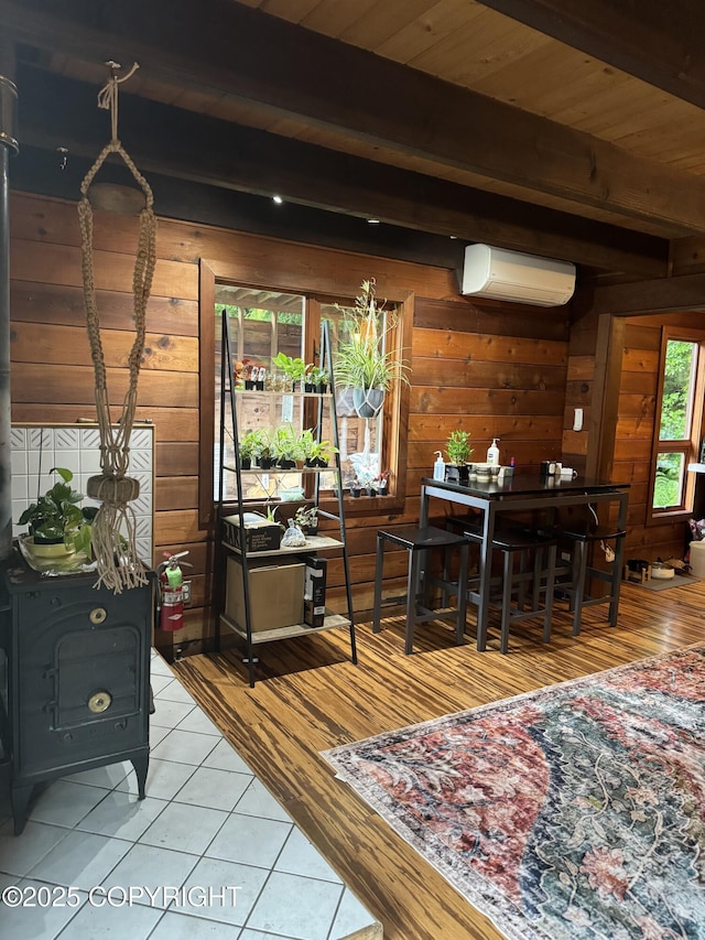 interior space featuring a wood stove, wood walls, beam ceiling, and a wall mounted air conditioner